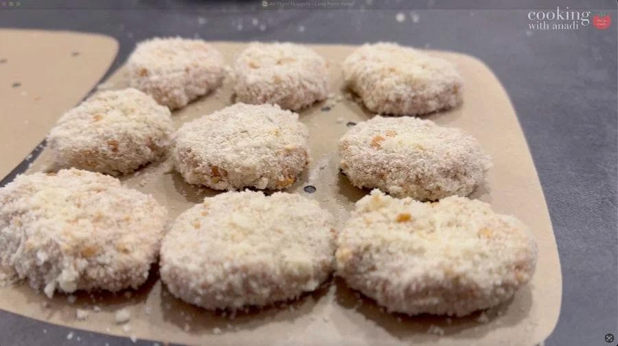 Nine breaded chicken nuggets on parchment paper, coated in golden breadcrumbs, ready for air frying.