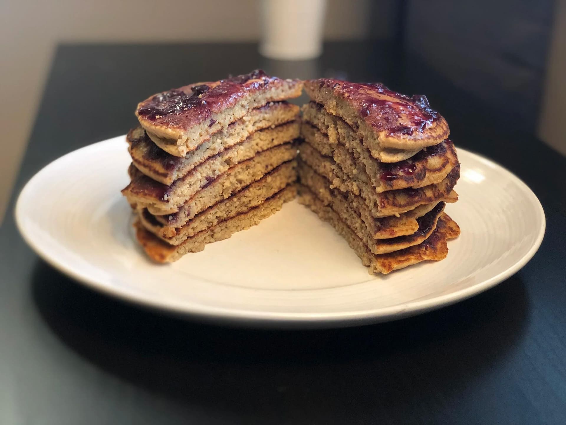 Stacked peanut butter and jelly pancakes with caramelized tops on a white plate, cut to show layers inside.