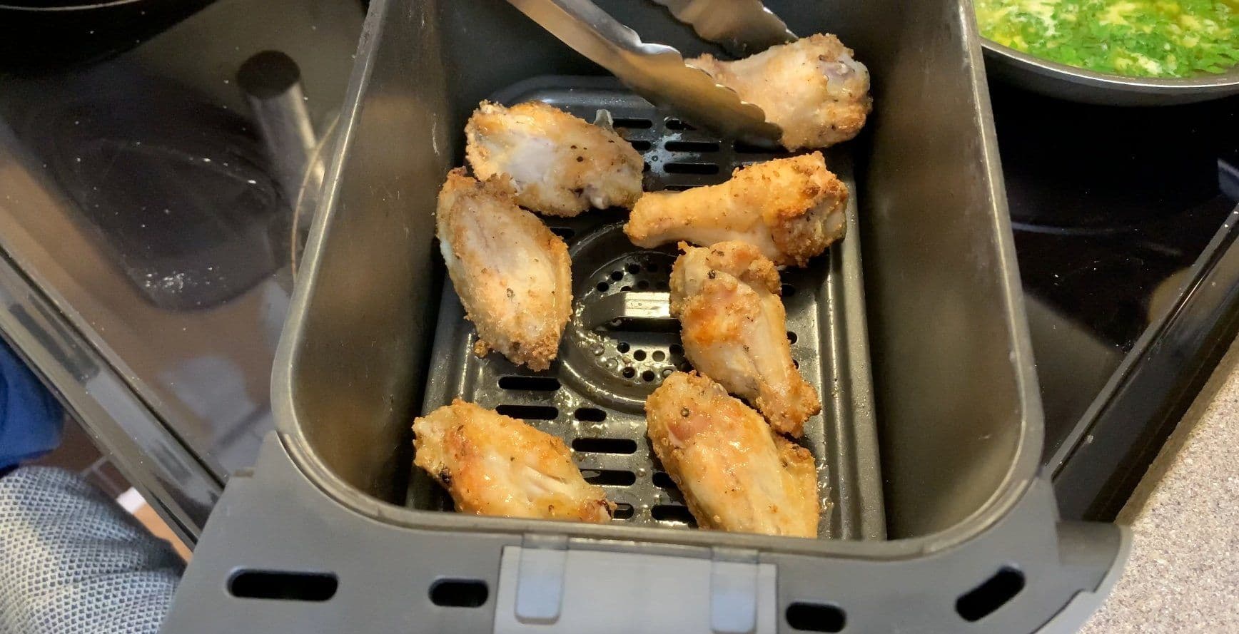 Cooked chicken wings in air fryer basket after 26 minutes, golden brown and ready to toss in sauce.