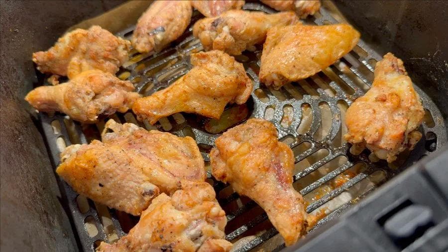 Golden and crispy chicken wings in air fryer basket after cooking at 400°F until deeply browned.