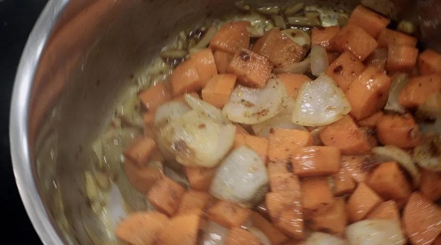 Simmering carrots and onions in a pot during the cooking stage of carrot and ginger soup.