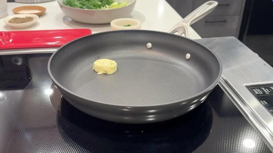 Melting garlic-chive butter in a dark skillet on the stovetop, ready for sautéing leeks and kale.