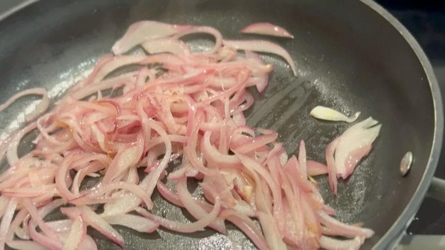 Sliced pink onions sautéing in a pan with melted butter on medium heat