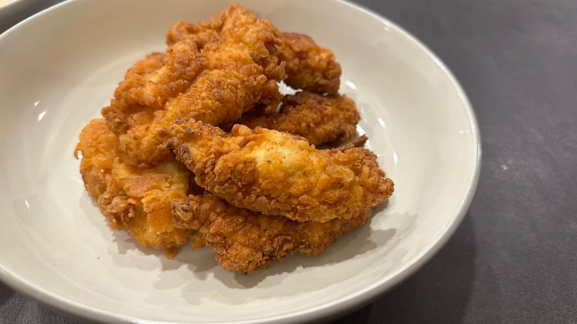 Golden-brown crispy fried chicken tenders piled on a white plate