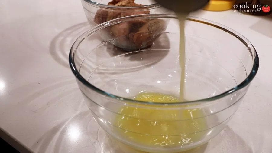 Pouring mojo marinade of garlic, citrus juice, and olive oil over chicken thighs in a glass bowl.
