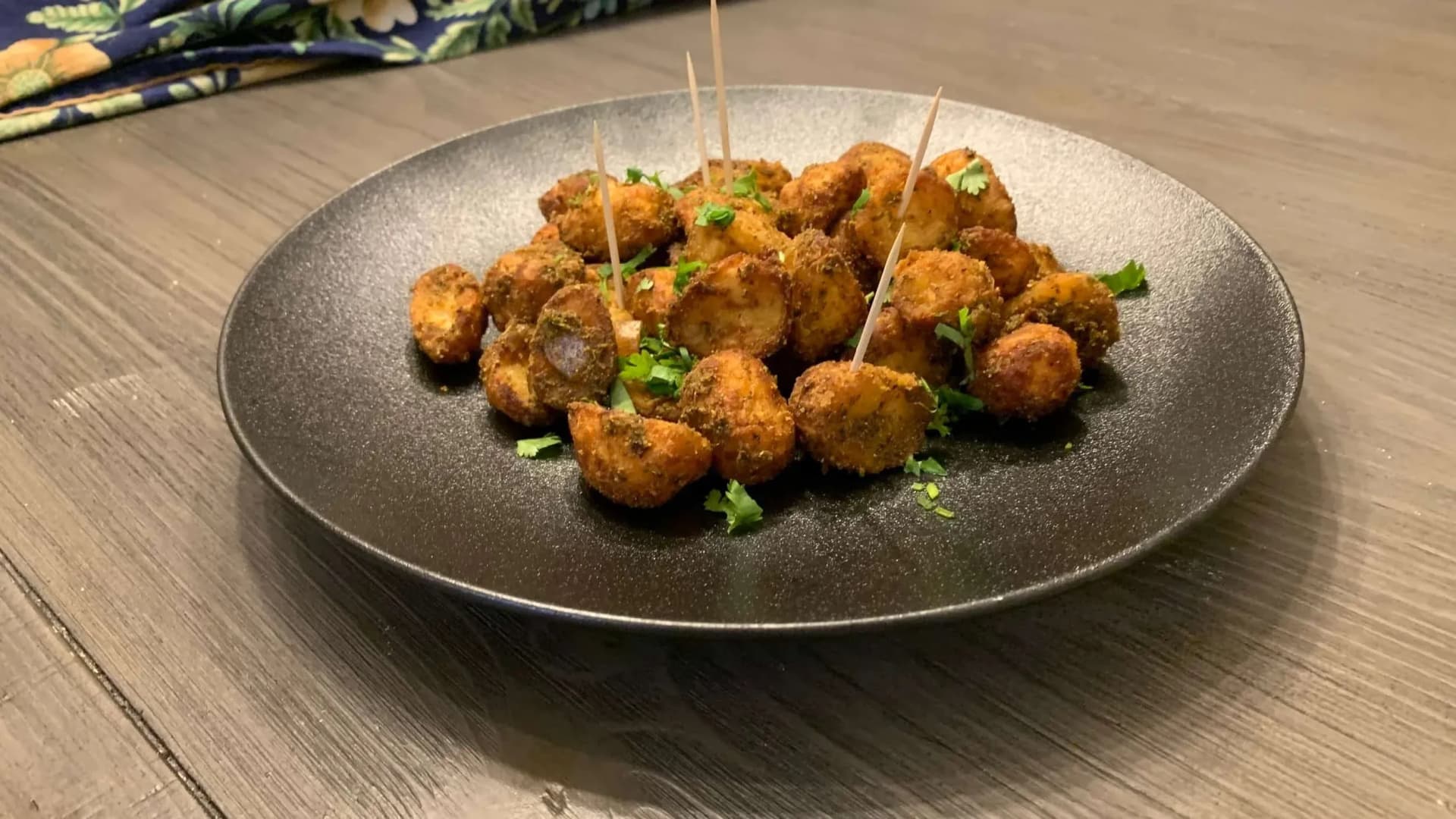 Air fryer baby potatoes with golden-brown crispy coating, garnished with fresh cilantro and served with toothpicks on a dark plate.