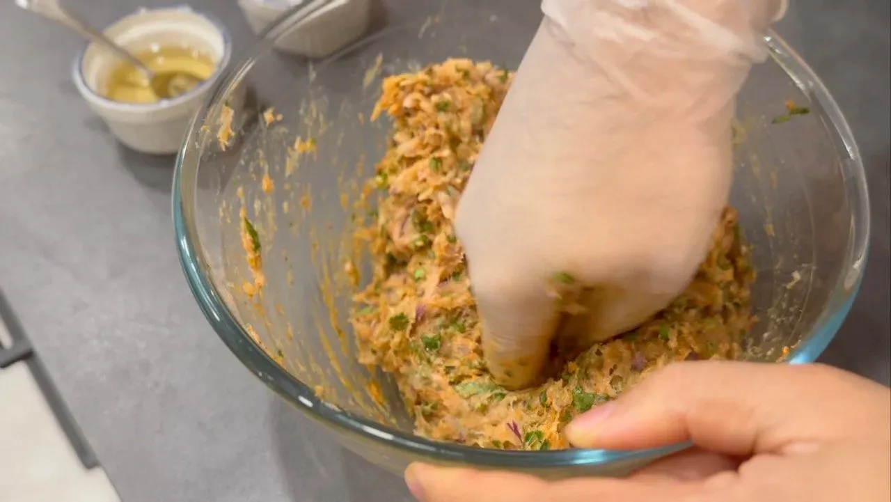 Hands mixing chicken momo filling ingredients in a glass bowl with visible herbs and spices.