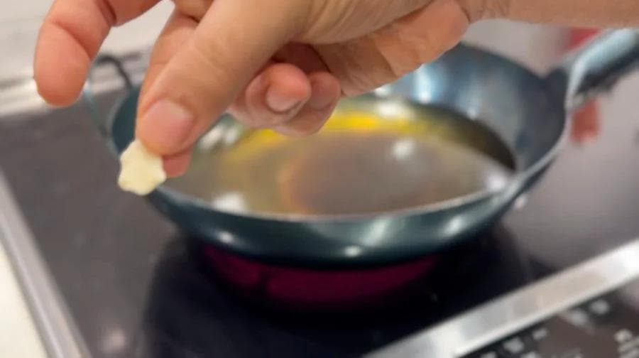 Hand dropping small piece of dough into hot oil in a wok to test temperature for frying beavertails.