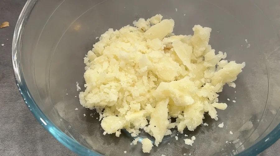 Scooped potato flesh in a glass bowl, fluffy and crumbly, ready for filling preparation.
