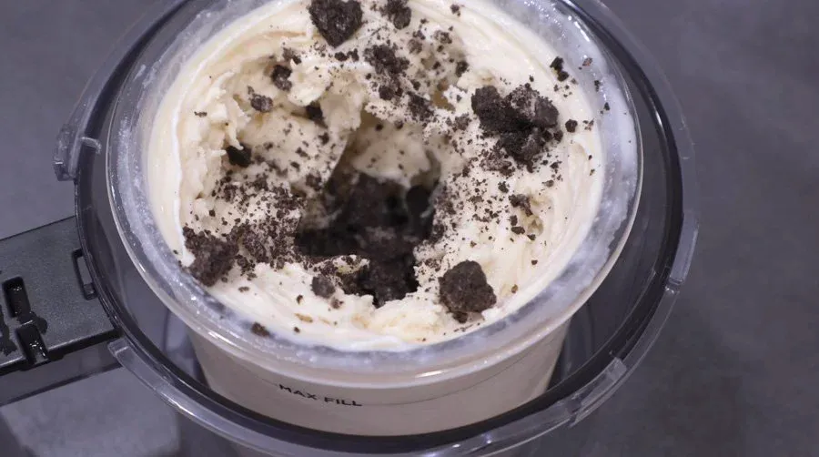 Soft serve ice cream base with crushed Oreo cookies mixed in, shown in ice cream maker container.