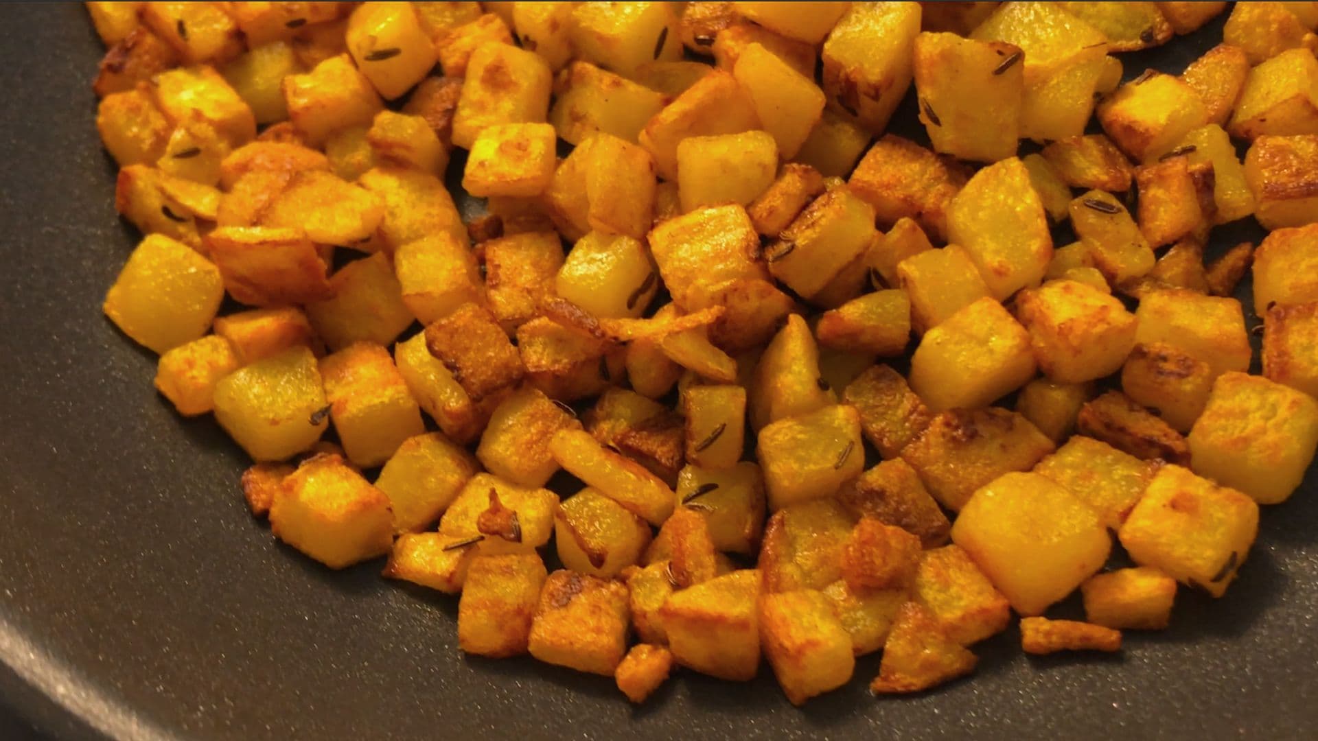 Crispy golden-brown diced potatoes in a pan, cooked until edges are caramelized and cubed pieces are tender.