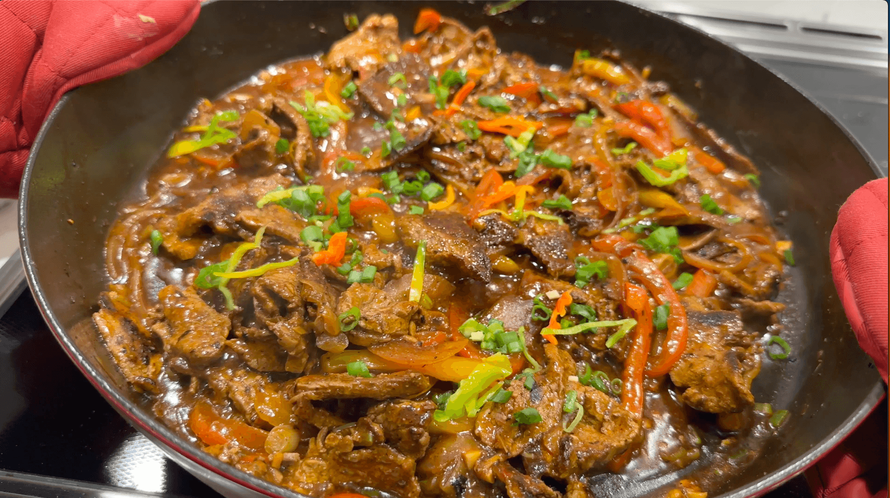 Sizzling Jamaican pepper steak with sliced beef, onions, and peppers in savory brown sauce, garnished with green onions.