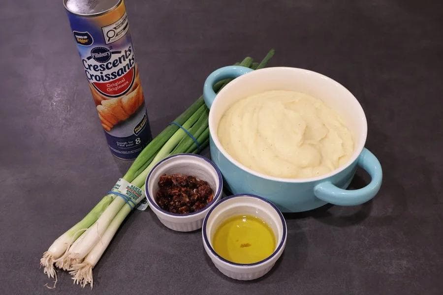 Ingredients for air fryer mashed potato pinwheels: crescent rolls, mashed potatoes, green onions, sun-dried tomatoes, and olive oil.