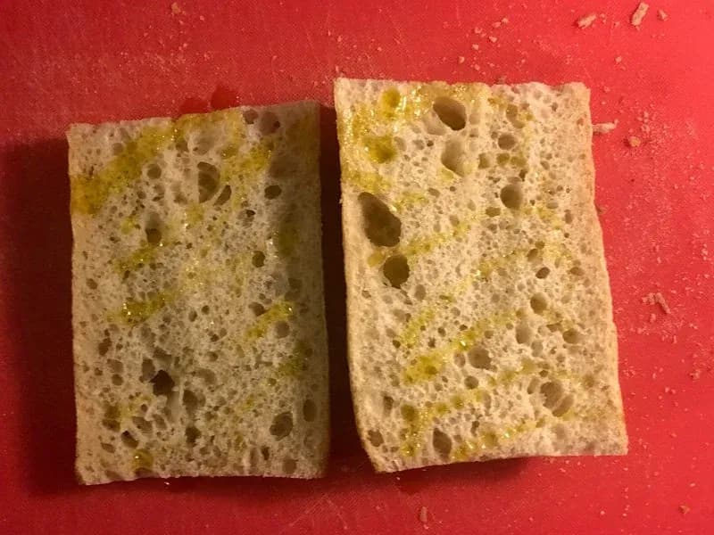 Two toasted ciabatta bread halves with olive oil, showing a golden-brown, crispy texture with visible air pockets.