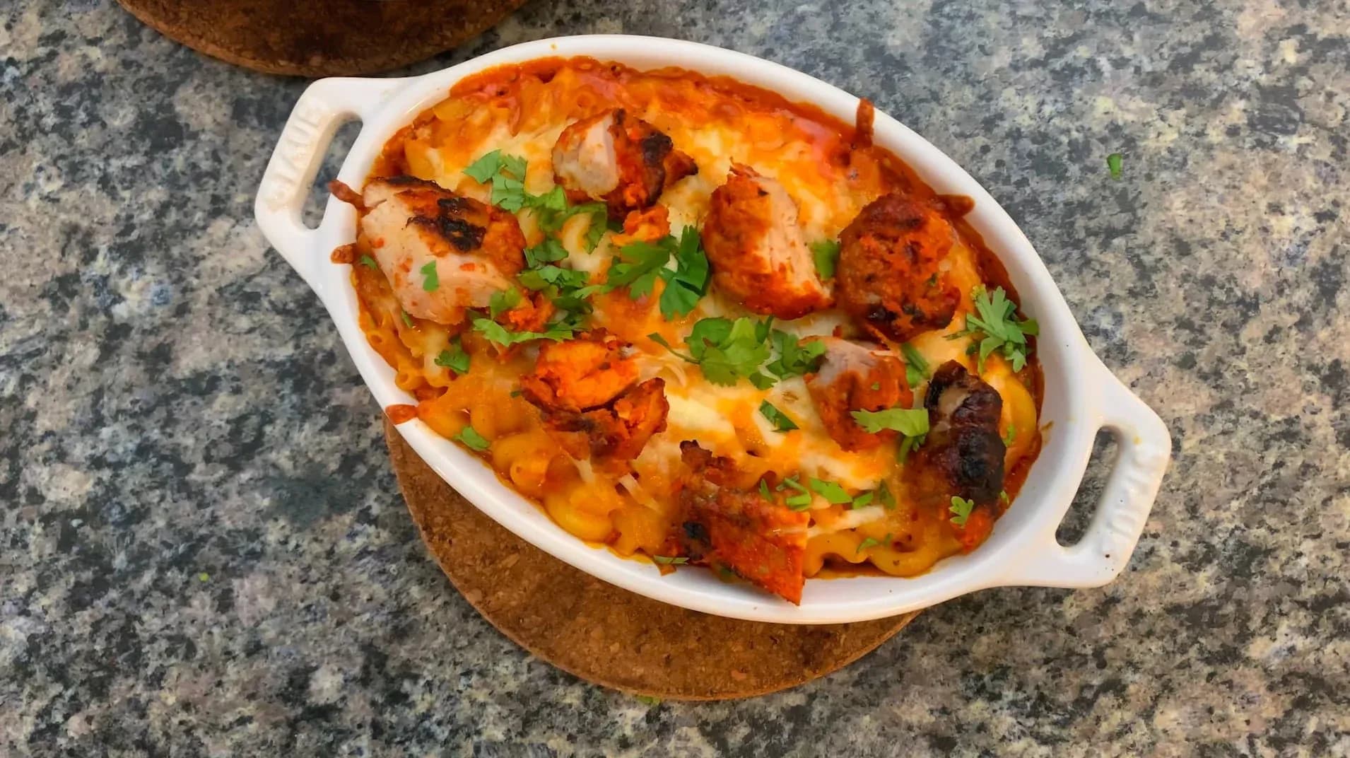 Butter Chicken Mac and Cheese in a white oval baking dish, topped with melted cheese and fresh cilantro garnish.