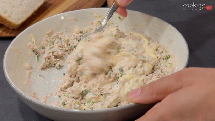 Mixing tuna salad with dill pickles in a white bowl, showing creamy texture with herbs and ingredients combined.