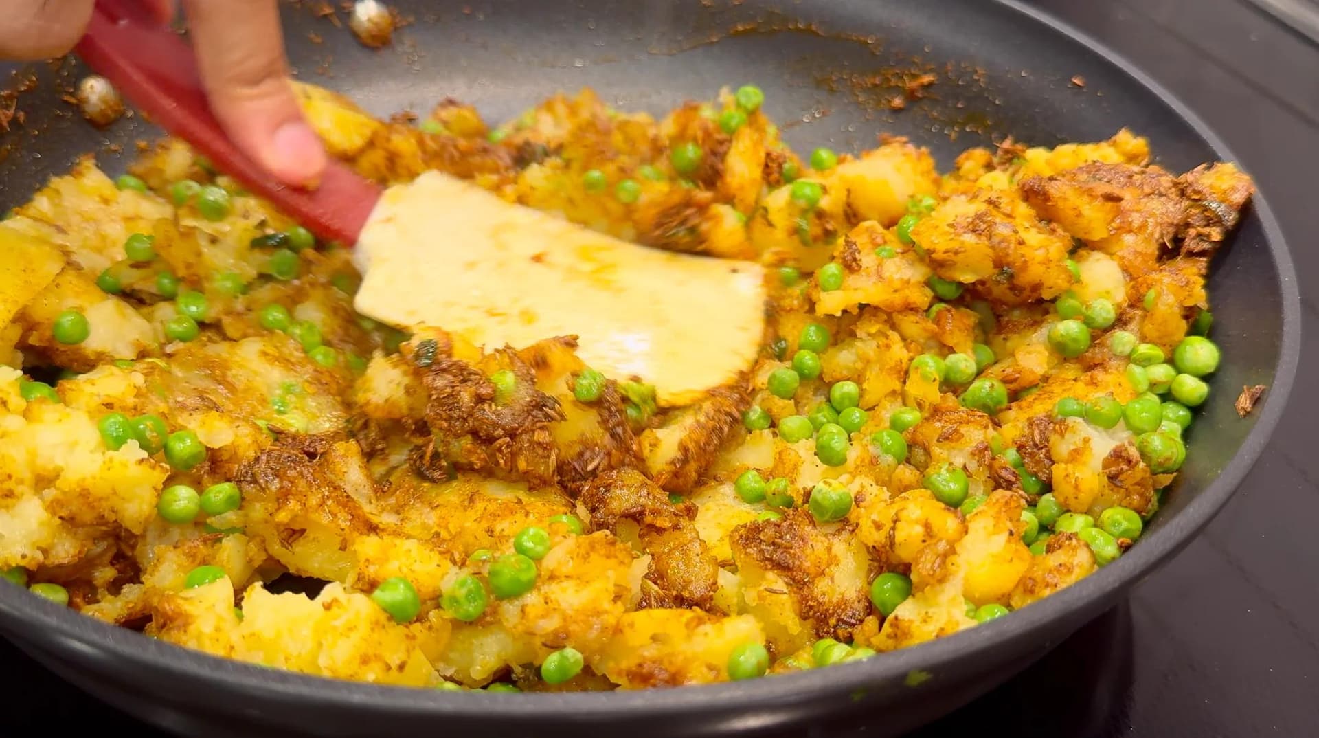 Potato samosa filling in a pan with peas, spices, and melting butter being stirred together.