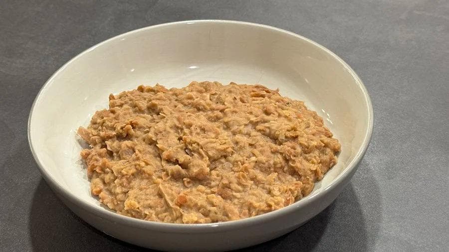 Homemade refried beans in a white bowl, showing a thick, textured paste with a tan and golden brown color.