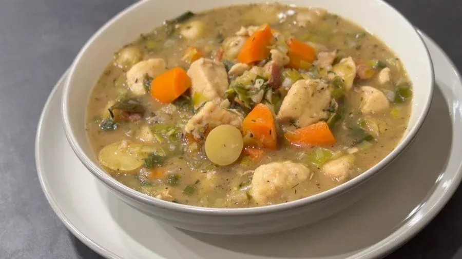 Creamy Country Harvest Chicken Stew with tender chicken pieces, carrots, potatoes, and peas in a rich broth, served in a white bowl.