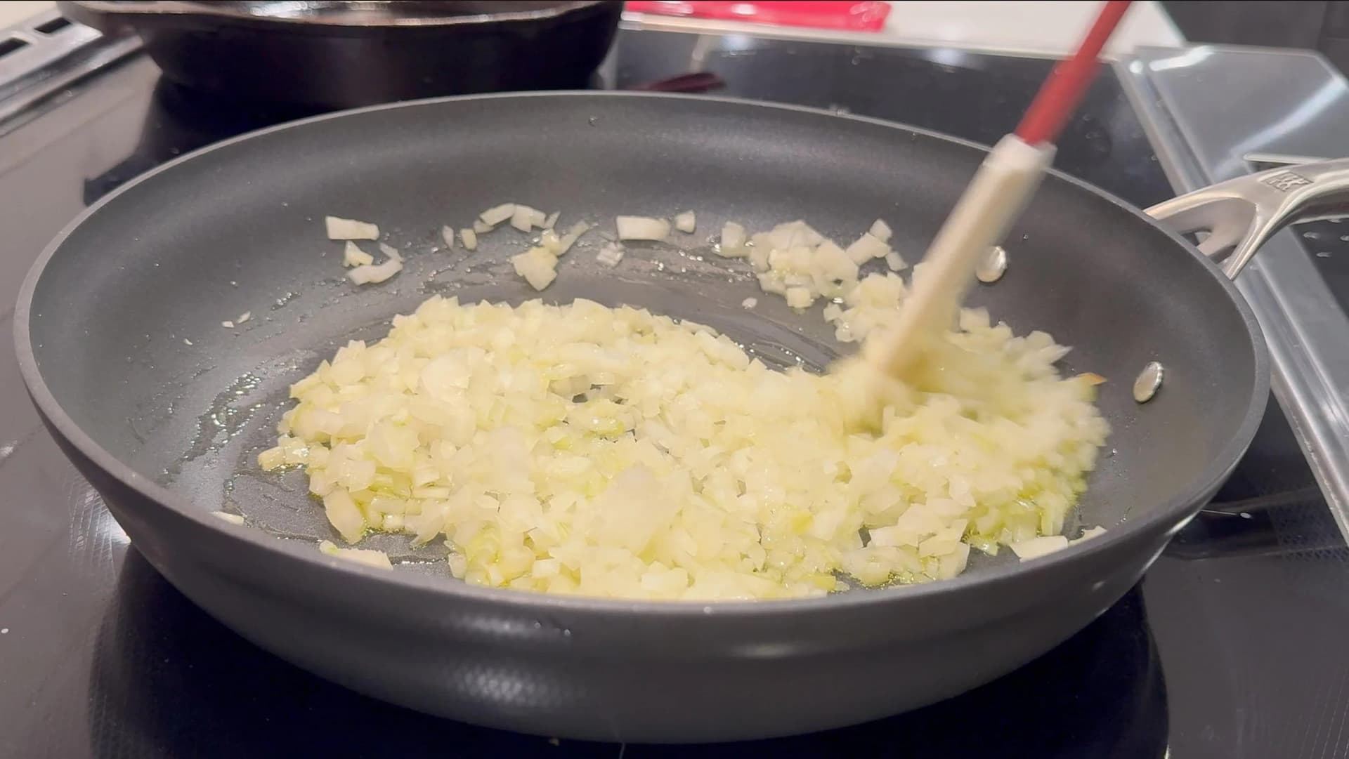 Diced onions sautéing in a dark nonstick skillet, stirred with a wooden spoon until soft and translucent.