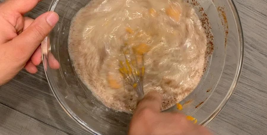 Whisking pumpkin puree into custard mixture in a glass bowl for bread pudding.