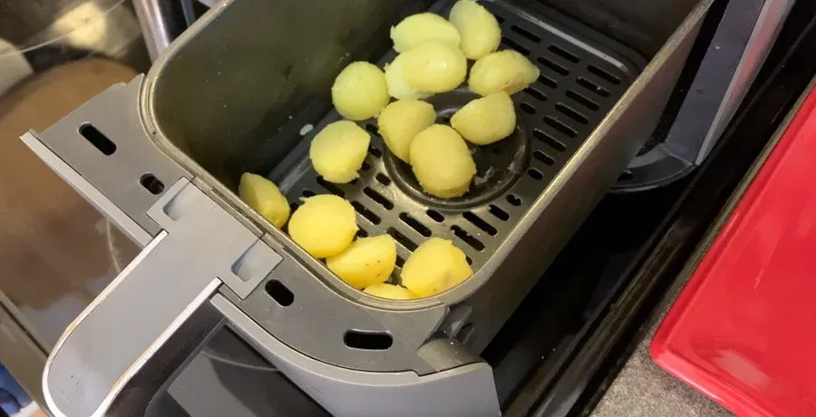 Baby potatoes coated in olive oil in an air fryer basket, ready to cook at 390°F.