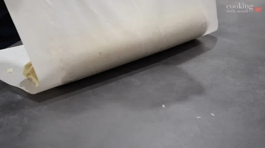 Parchment paper being used to roll filled dough into a tight log for Croatian cheese pastry.