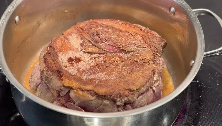 Seared beef chuck roast in a stainless steel pot with a golden-brown crust on all sides.