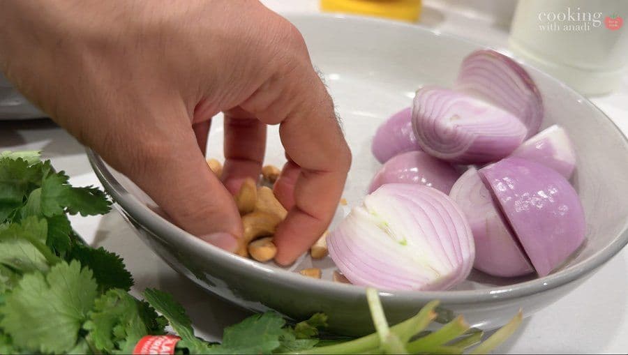 Hand adding ginger to bowl of sliced red onions for Balinese beef rendang spice paste.