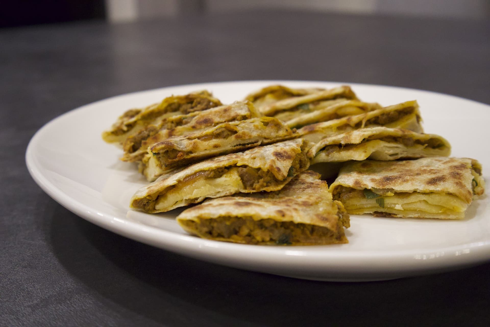 Golden-brown beef martabak triangles arranged on a white plate, showing crispy, folded pastry with visible filling.