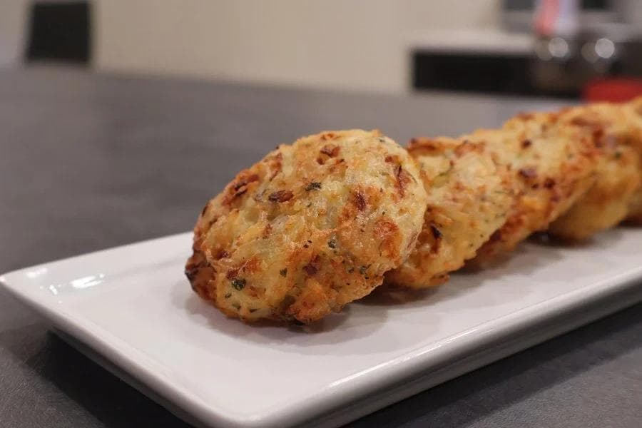Golden-brown Venezuelan cheese rice fritters arranged in a line on a white rectangular plate.