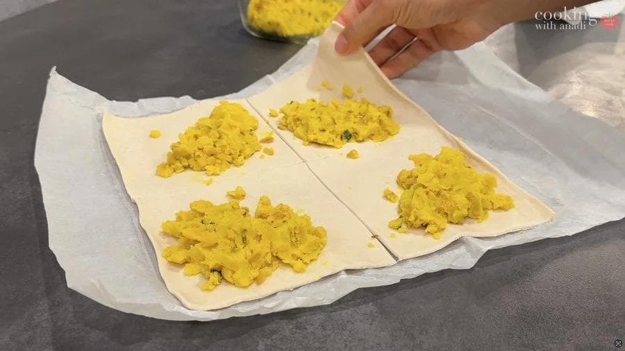 Folded puff pastry squares filled with yellow potato mixture on parchment paper, ready for air frying.