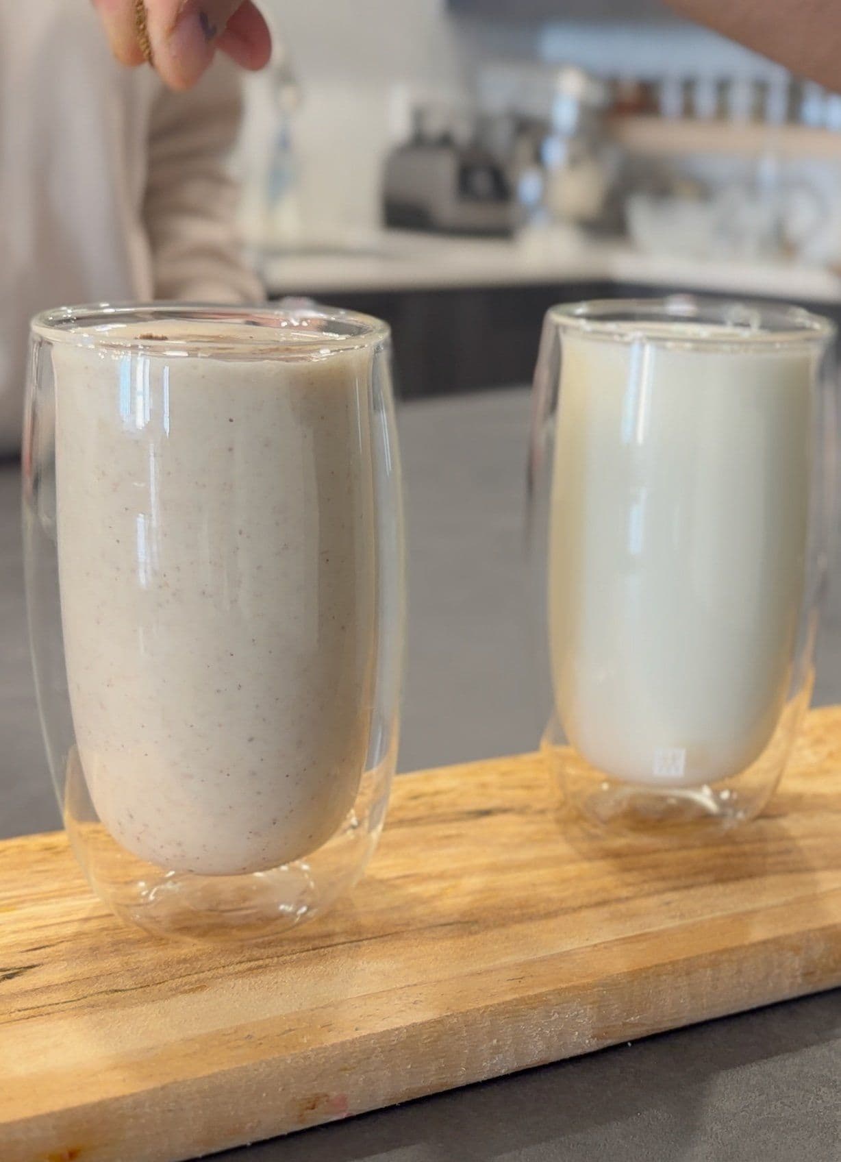 Two glasses of creamy mattha yogurt drink with visible spice garnish on a wooden board.