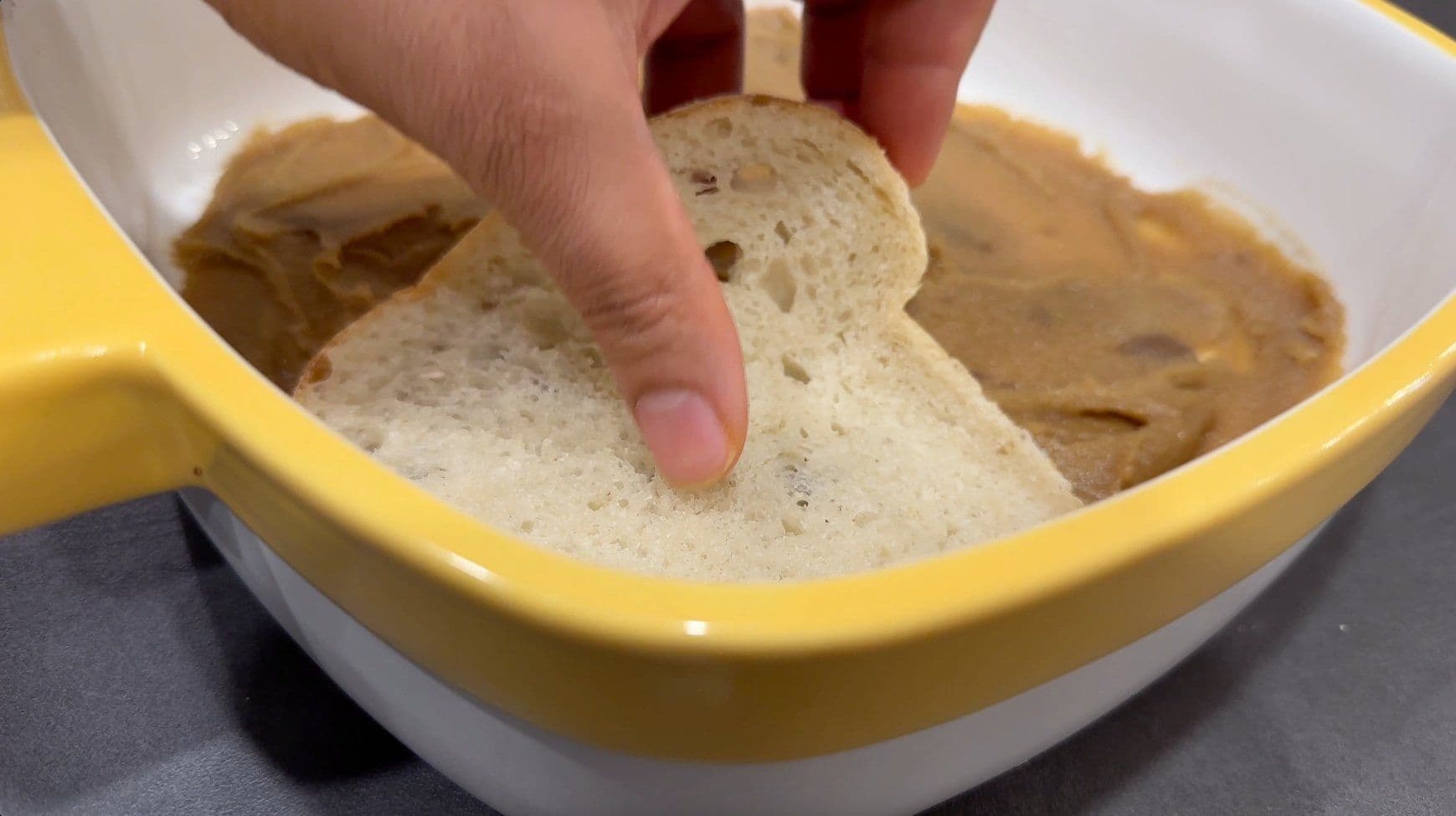 Hand dipping bread into egg-milk mixture in yellow casserole dish for French toast casserole.