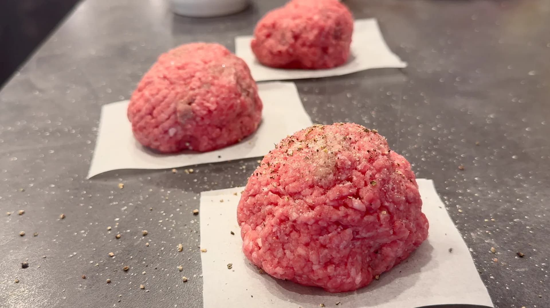 Three 6-ounce ground beef portions formed into balls on parchment paper squares, ready for seasoning and cooking.