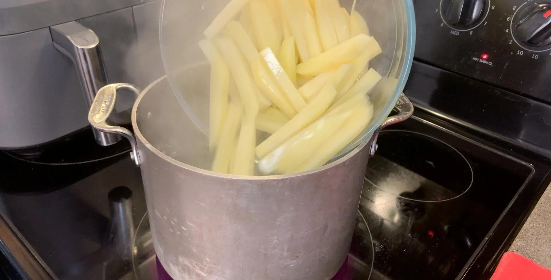 Partially cooked potato fries draining in a colander over boiling water on the stovetop.