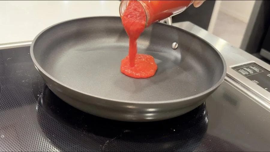 Red Korean sauce being poured from a jar onto a dark non-stick skillet pan.