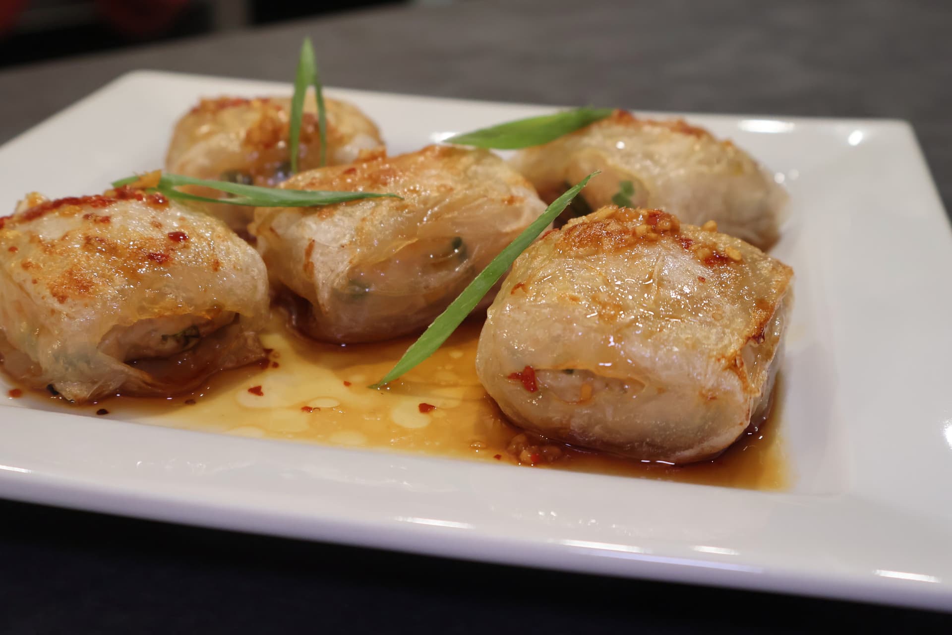 Four golden-brown seared chicken dumplings on a white plate with sauce, garnished with green onion slices.