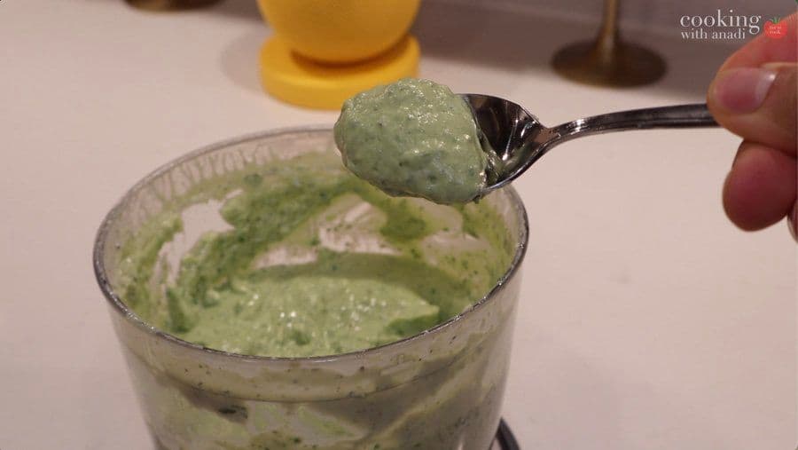 Spoonful of creamy avocado lime crema being held above a glass bowl of the finished sauce.