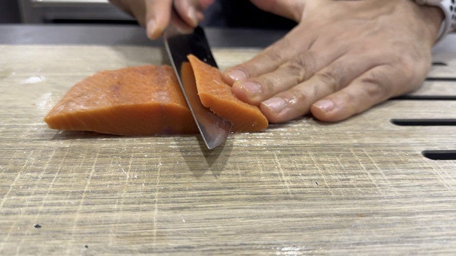 Chef slicing salmon sashimi-style with a sharp knife on a wooden cutting board for oshizushi.
