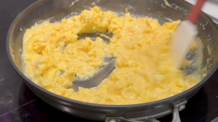 Scrambled eggs being cooked in a non-stick pan with a spatula, still slightly runny and creamy in texture.