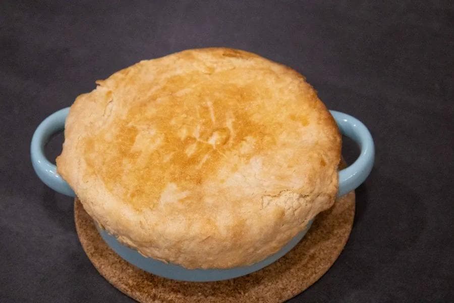 Golden-brown baked chicken pot pie with flaky top crust in a blue ceramic dish on cork trivet.