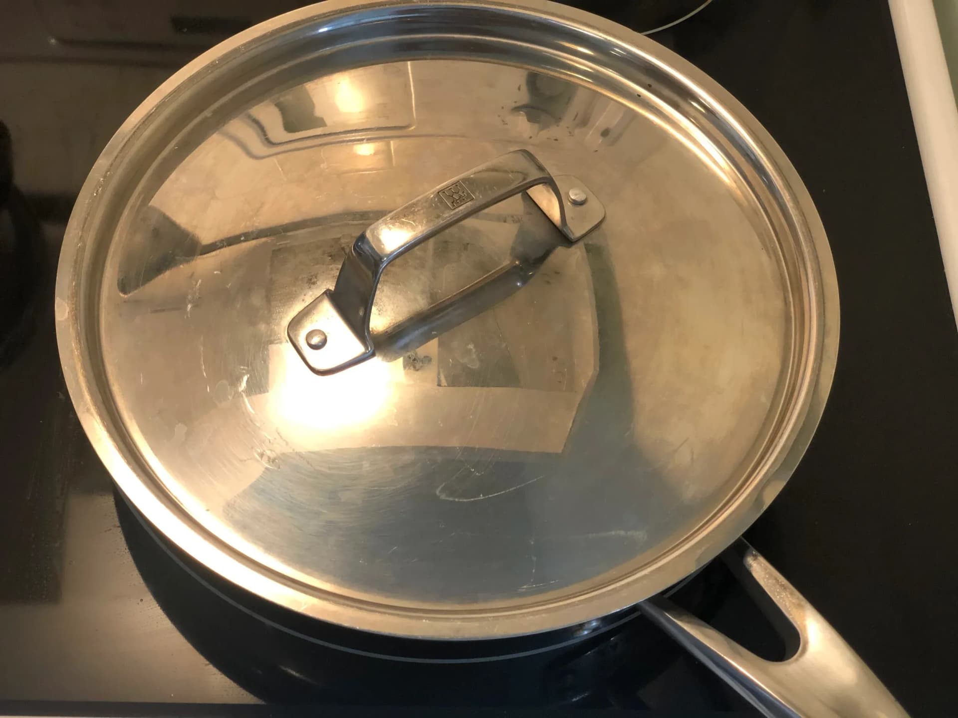Skillet with glass lid containing pasta mixture with melted cheese, resting off heat.