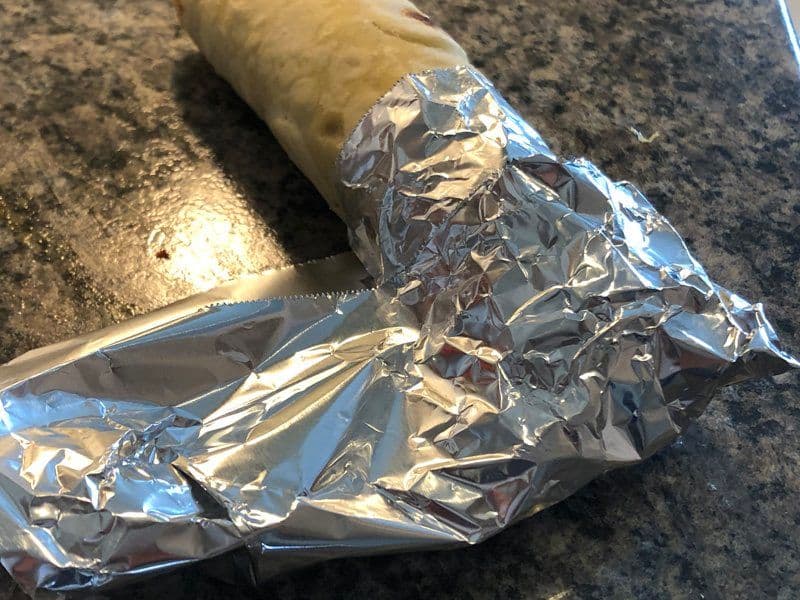 Chicken kathi roll wrapped in aluminum foil on a dark countertop, ready to serve.