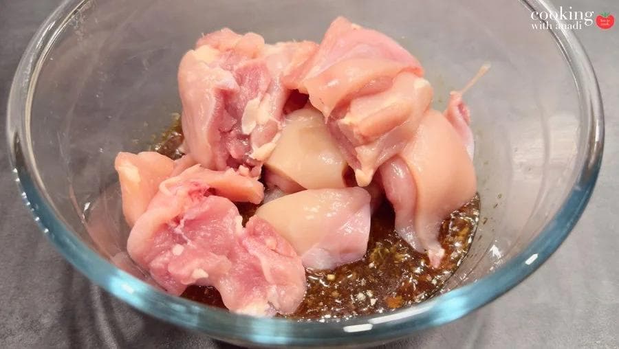 Raw chicken pieces in a glass bowl with dark Thai marinade of lemongrass, soy, fish sauce, and lime juice.