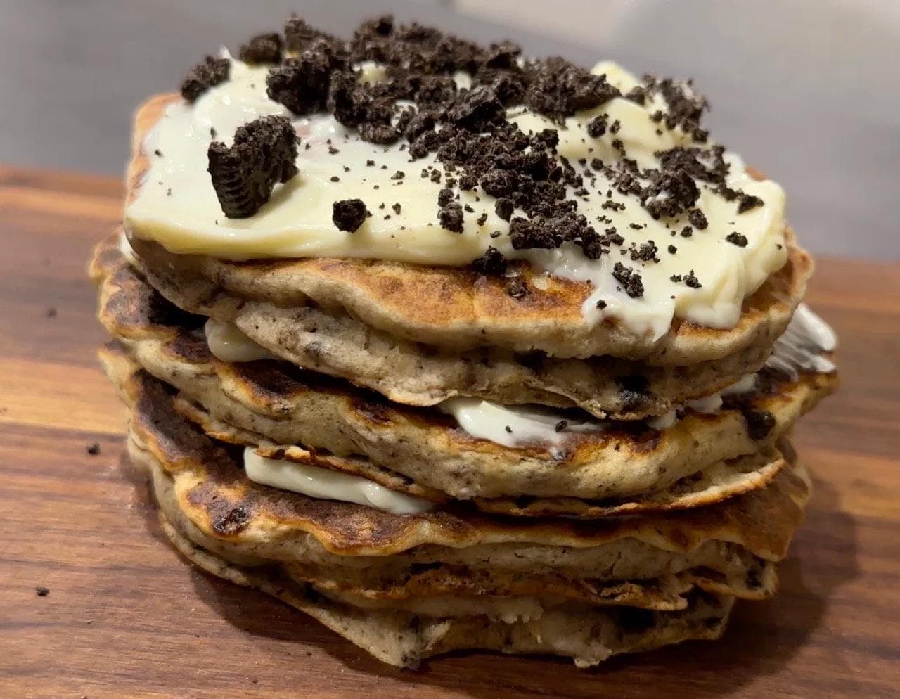 Stack of four gluten-free pancakes with cream cheese frosting and crushed Oreos on top.