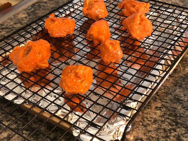 Chicken tikka pieces cooking on a wire rack lined with foil under the oven broiler, showing orange-charred marinade coating.
