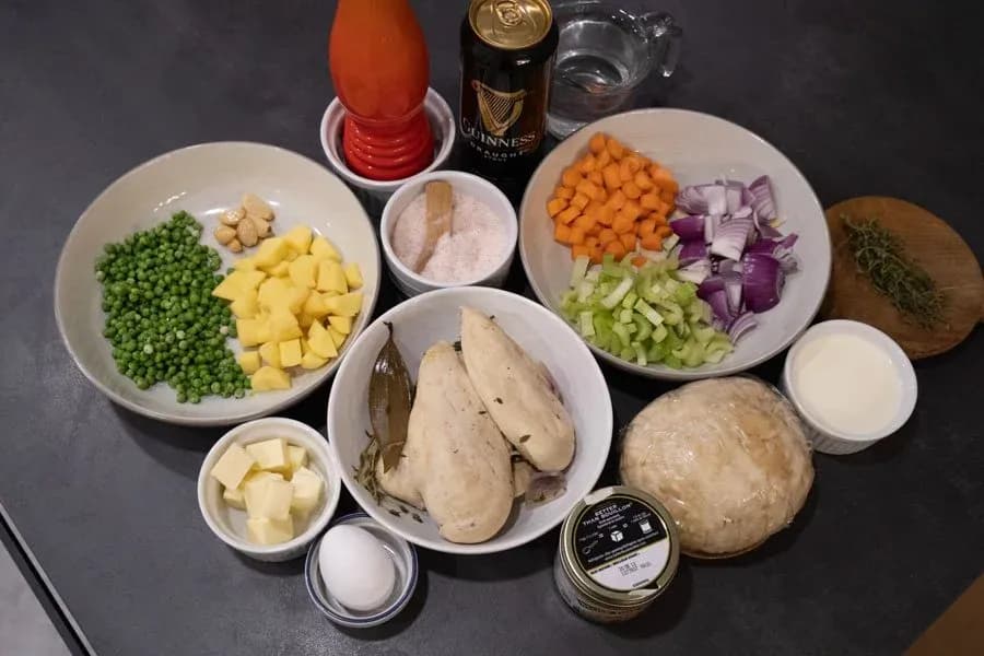 Ingredients laid out for Guinness Chicken Pot Pie including chicken breasts, vegetables, potatoes, peas, and a Guinness beer bottle.