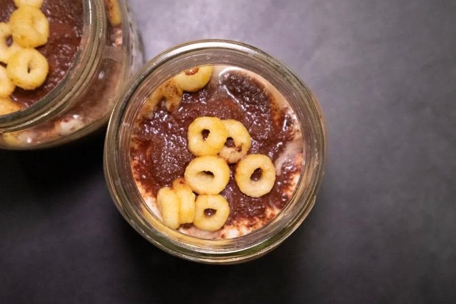 Two glass jars of chocolate tiramisu overnight oats topped with sliced almonds on a dark surface.
