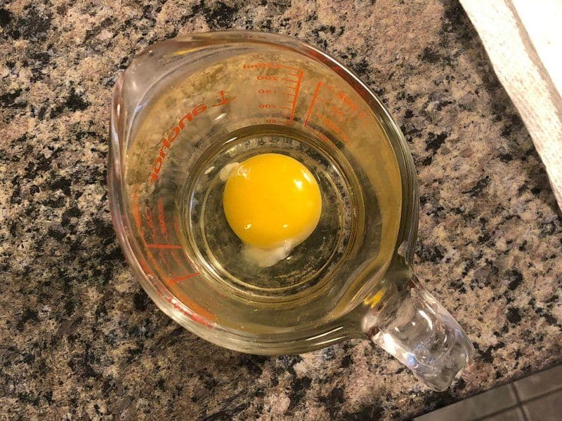 Raw egg in a glass measuring cup filled with water and vinegar, ready to be poached.